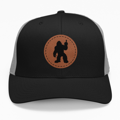 Preview of the 'Bigfoot Silhouette Middle Finger' leatherette patch on a custom hat, showcasing the bold design on an adjustable snapback.