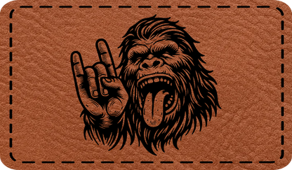 Close-up of the 'Bigfoot Rock Out' leatherette patch, featuring Bigfoot throwing rock horns with his tongue out, perfect for Sasquatch and music fans.