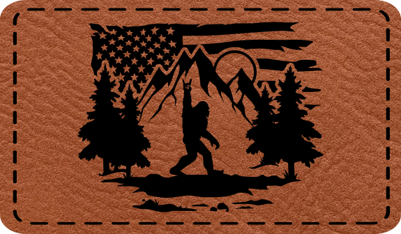 Close-up of the 'Bigfoot Flag Outdoors' leatherette patch featuring Bigfoot throwing rock horns in front of a mountain range with an American flag backdrop.