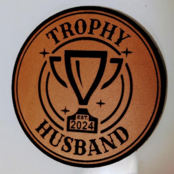 Close-up of the "Trophy Husband" leatherette patch featuring playful text.