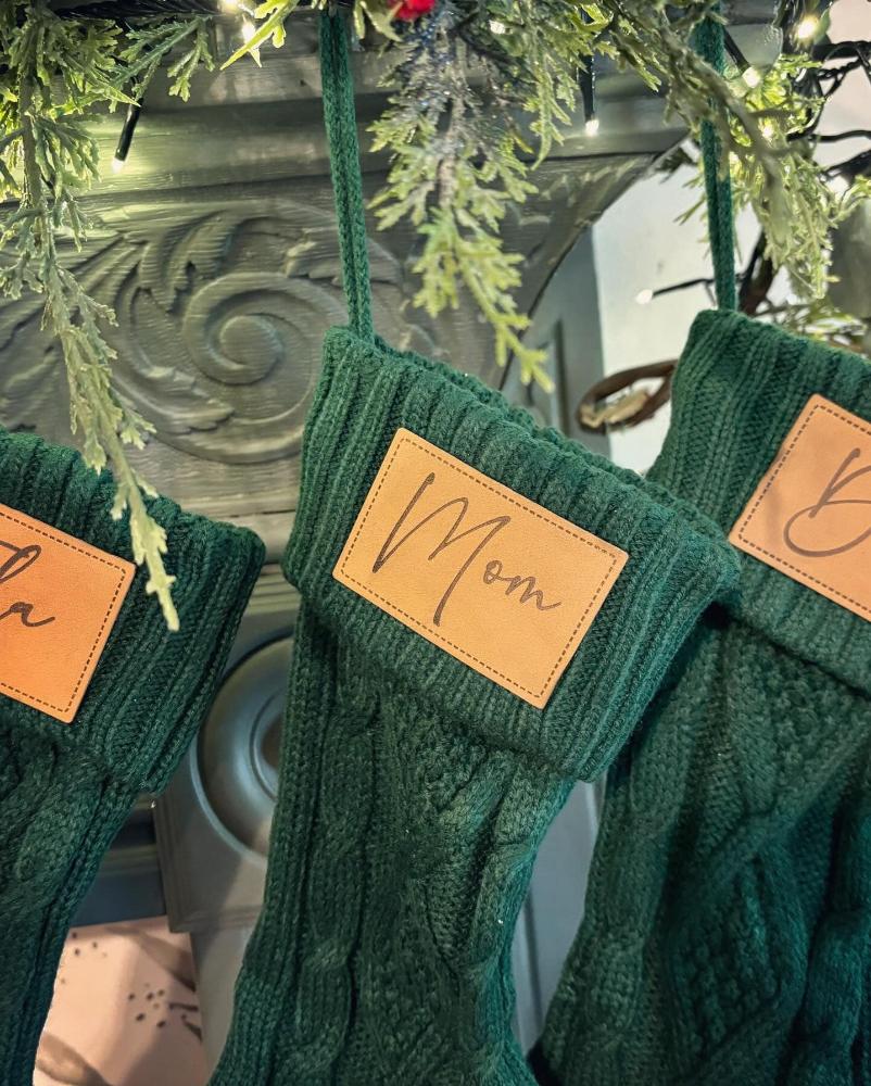 Personalized Knit Christmas Stocking hanging by the fireplace, displaying the laser-engraved name patch and cozy cable knit design.